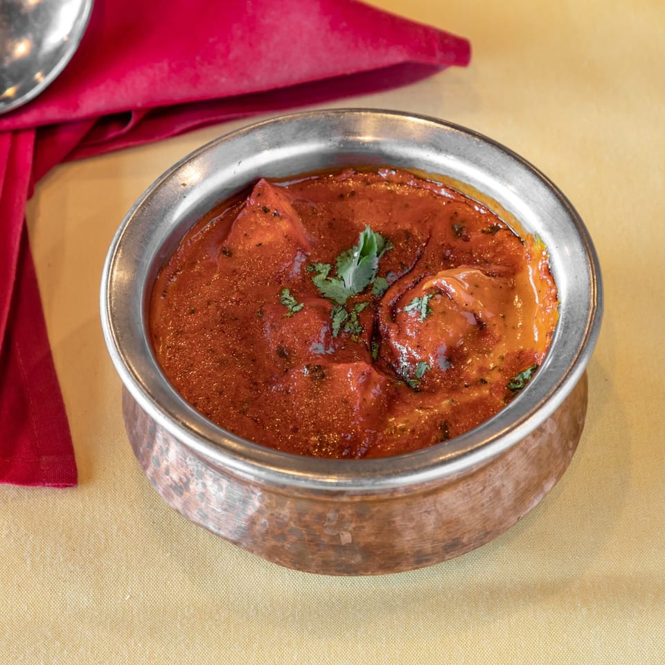 Indian butter chicken in a copper bowl, garnished with cilantro, on a yellow tablecloth.