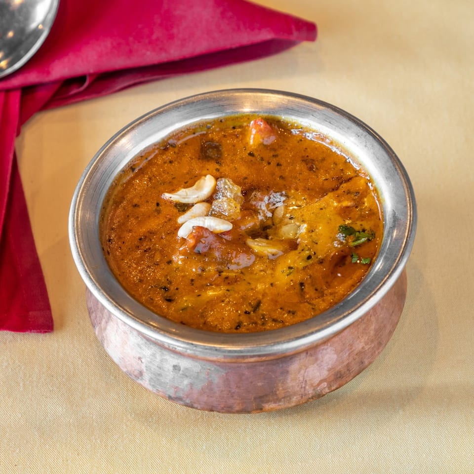 Indian Korma curry with cashews and raisins in a copper bowl on a yellow tablecloth.