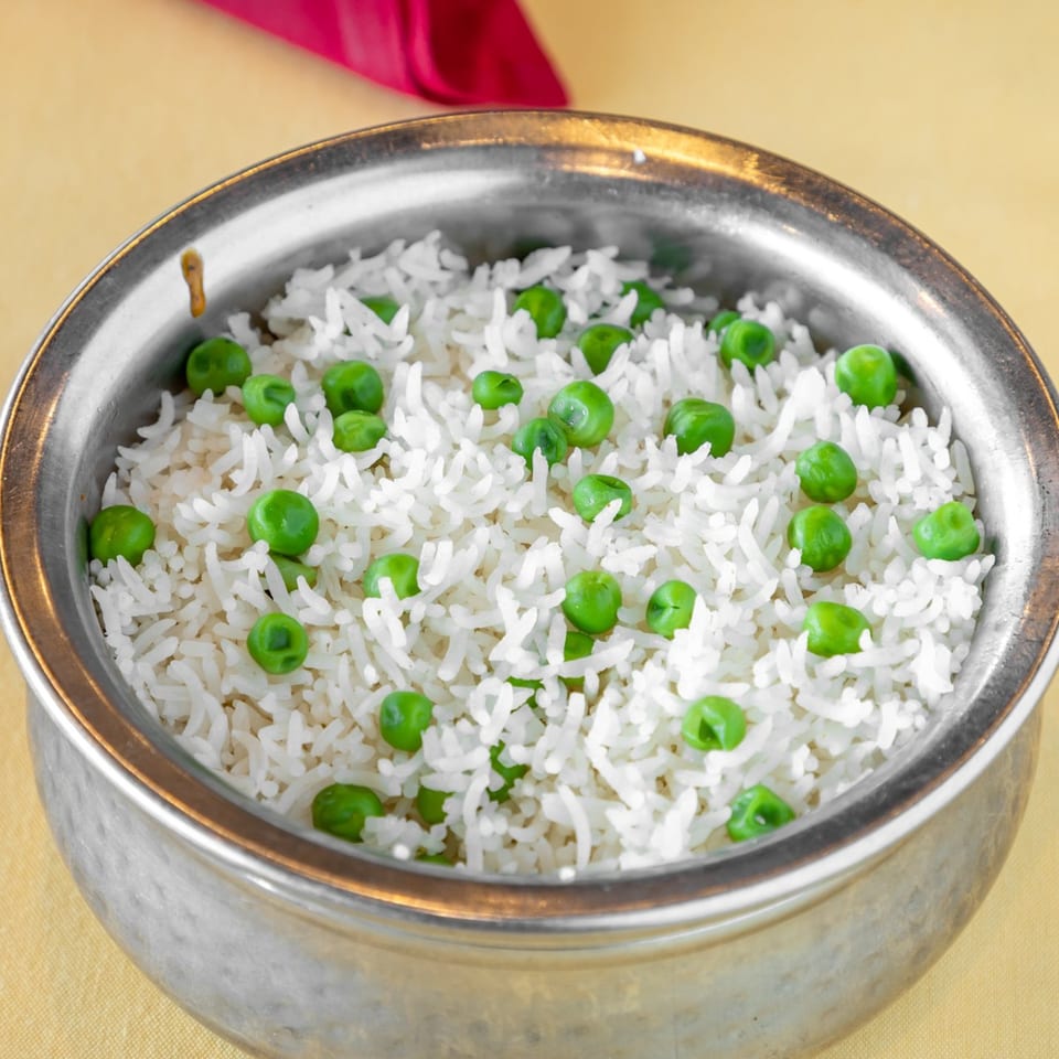 Peas Pulao, white rice with green peas, served in a silver bowl on a yellow tablecloth.