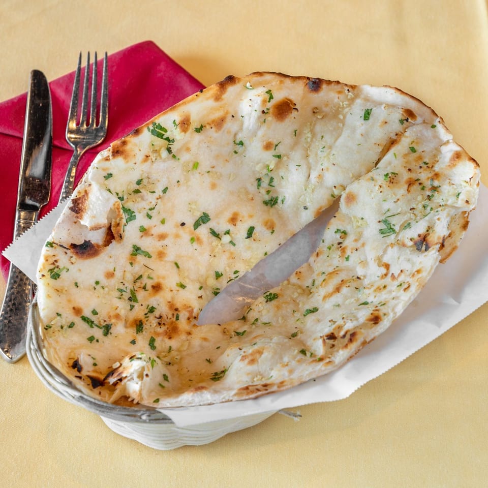 Garlic naan bread in a basket with a knife and fork on a red napkin at Himalayan Kitchen.