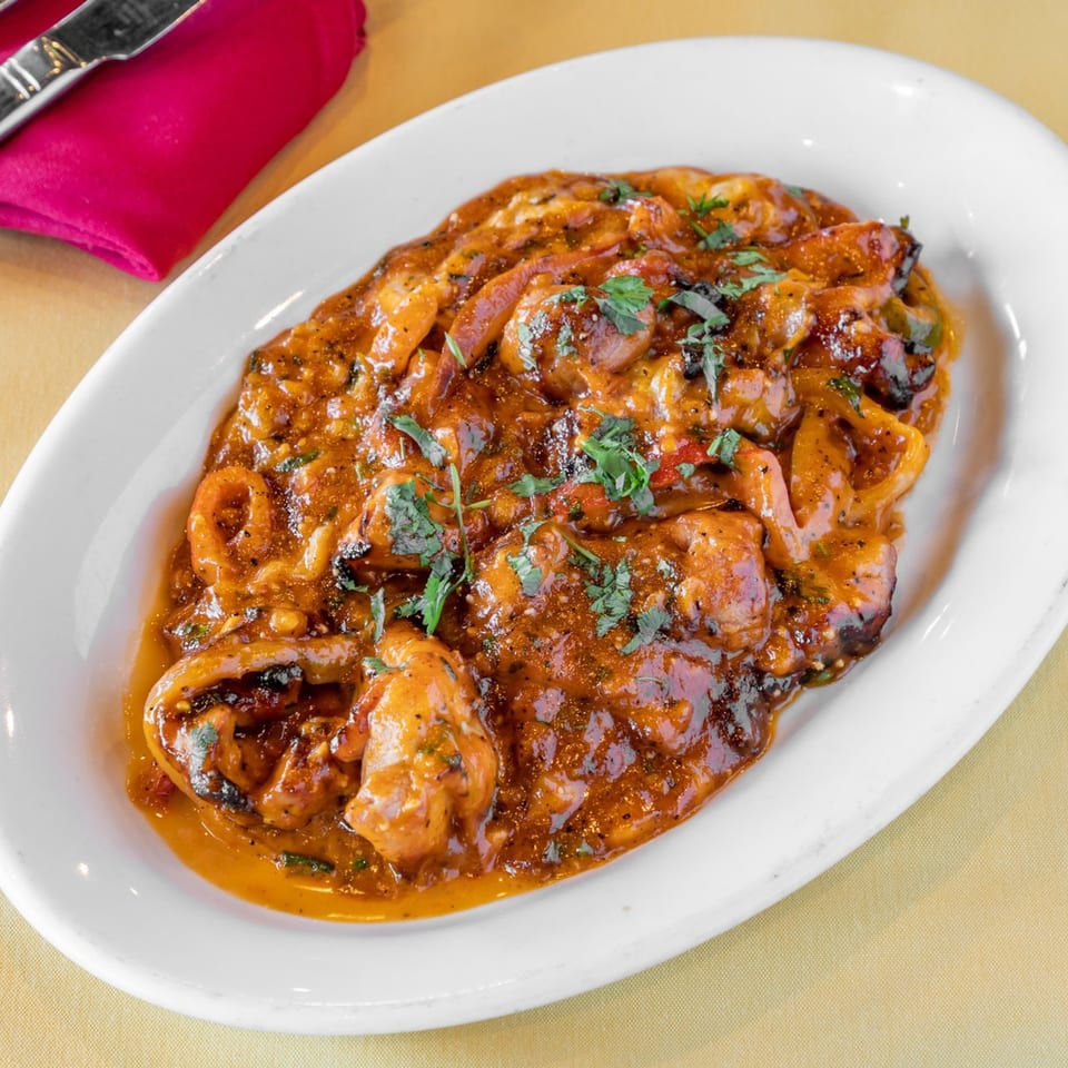 A white oval plate filled with Indian chili chicken, garnished with fresh cilantro.