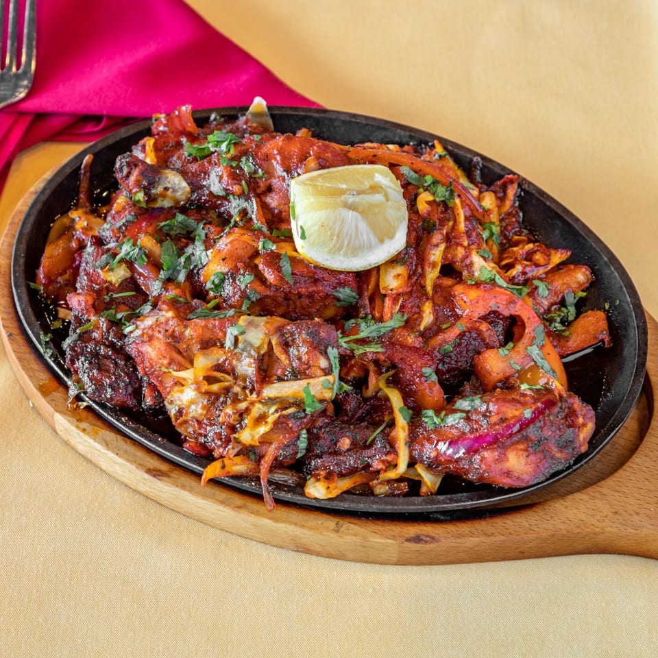 Indian chicken tikka sizzler with onions, peppers, and a lemon wedge on a cast iron plate.