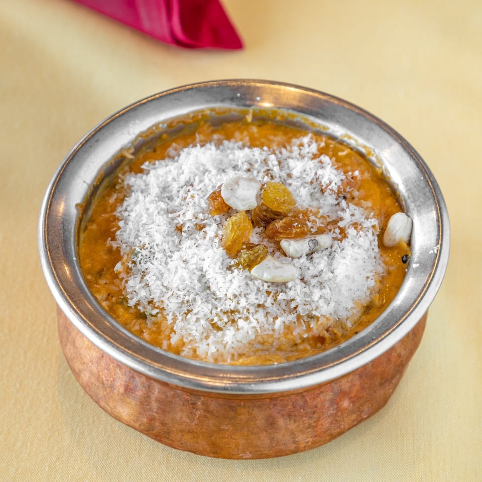 Indian dessert in a copper bowl, topped with shredded coconut, raisins, and nuts.