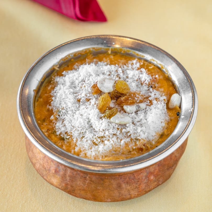 Indian dessert in a copper bowl, topped with shredded coconut, raisins, and nuts.